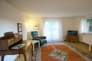 Ein Wohnzimmer mit einem Holztisch, einem grünen Sessel, einem Fernseher und einem gemusterten Teppich.
