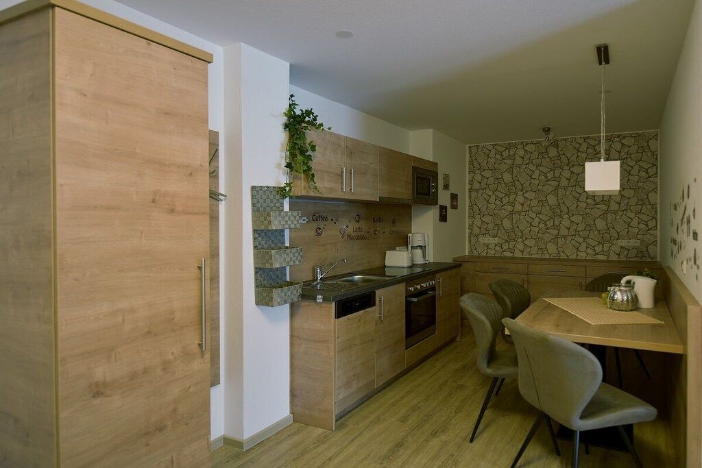 Une cuisine compacte dotée de meubles en bois, d’un four encastré, d’une machine à café et d’un coin repas avec une table et des chaises.