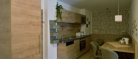 Cocina compacta con armarios de madera, horno empotrado, cafetera y zona de comedor con mesa y sillas.