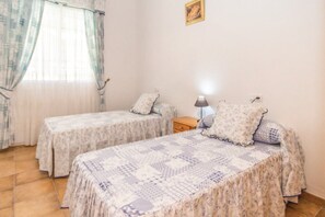 Una habitación con dos camas, una mesita de noche, una lámpara y un ventanal con cortinas.