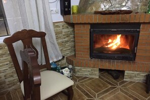 Ein Kamin mit Feuer, ein Holzstuhl und eine Steinwand.