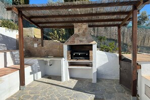 Eine Außenküche mit Stein Arbeitsplatte, Spüle und Grill unter einer Holz-Pergola.