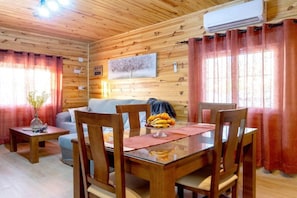 Ein Holzinterieur mit Esstisch, Stühlen, einer Couch und einer Wand-Klimaanlage.