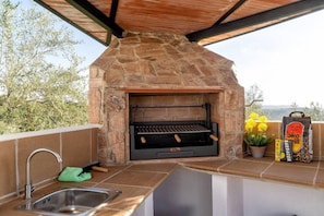 Une cuisine extérieure dotée d’un barbecue en pierre, d’un évier et d’un sac à barbecue.
