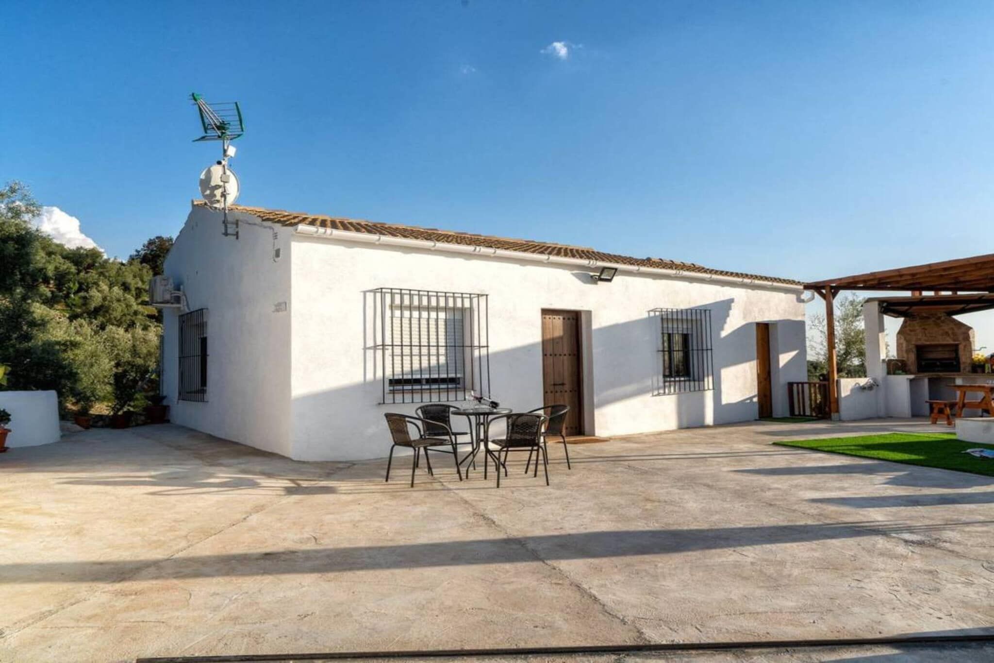 A white building with a tiled roof, a small patio with a table and chairs, and a wooden pergola structure.