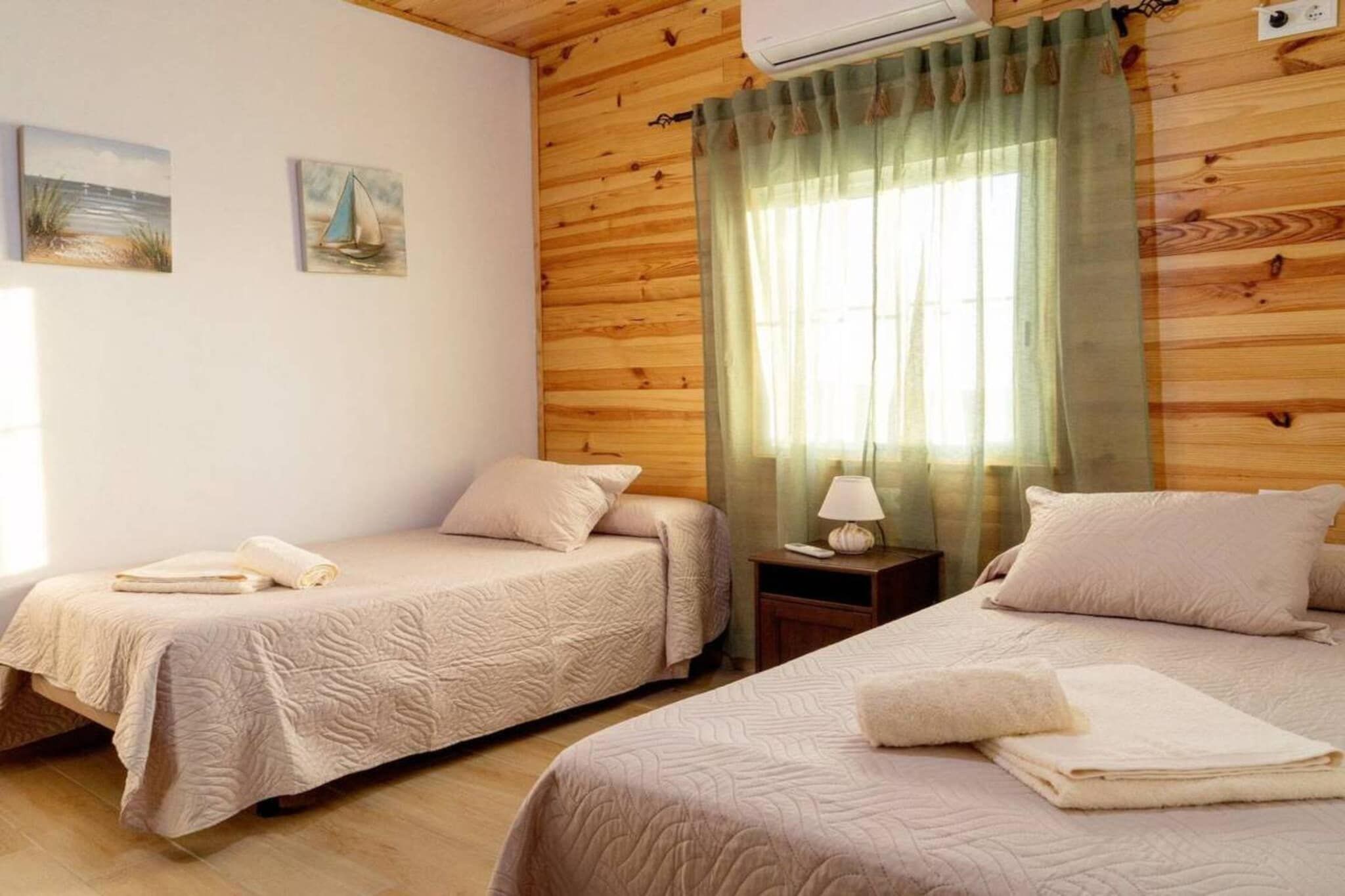 A room with two beds, a nightstand, a lamp, and a window with curtains.
