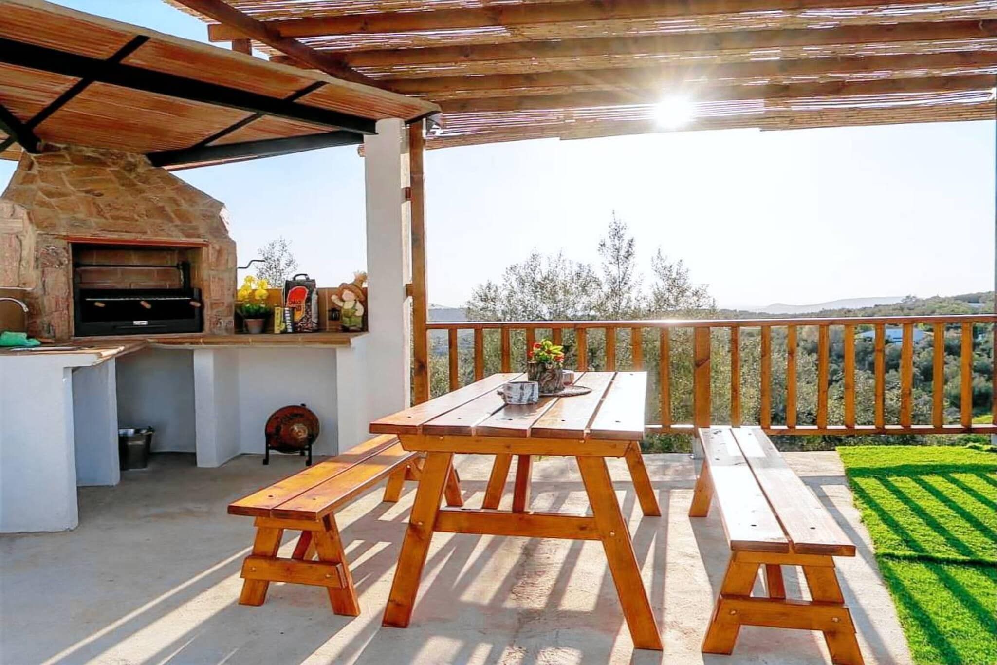 Une terrasse extérieure avec un four en pierre, des bancs en bois et une table agrémentée d’un vase de fleurs.