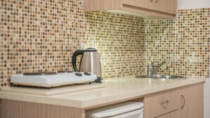 A kitchen with a tiled backsplash, a kettle, a sink, and wooden cabinets. - Stefania Apartment (Hersonissos)