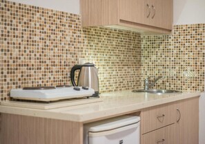 A kitchen with a tiled backsplash, a kettle, a sink, and wooden cabinets. - Stefania Apartment (Hersonissos)