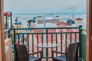 A balcony with two wicker chairs and a small round table, overlooking a beach with buildings in the background. - Stefania Apartment (Hersonissos)