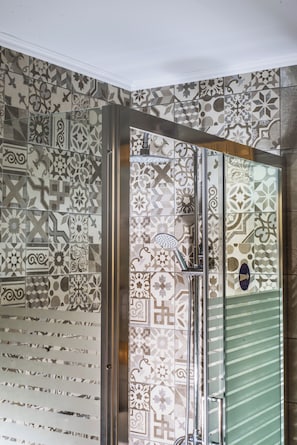 A bathroom with patterned tiles, a shower area, and a glass door. - Stefania Apartment (Hersonissos)