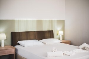 Una habitación de hotel con una cama grande, dos mesitas de noche con lámparas, y toallas ordenadas sobre la cama.