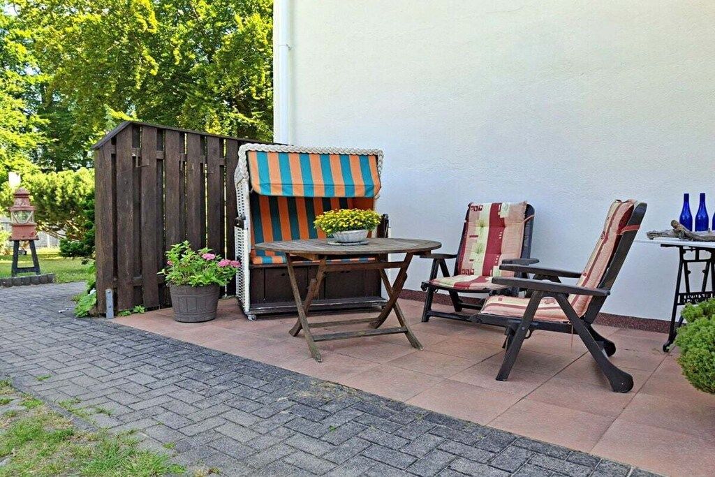 Ein Außenbereich mit Holztisch und -stühlen, einer kleinen Holzhütte mit Streifenmarkise und Blumentöpfen.