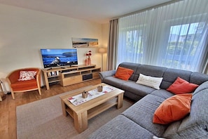 A modern living room with a grey sofa, a wooden coffee table, a television, and a bookshelf. - Holiday apartment 3.02 Island beach (Ahlbeck (Seebad))