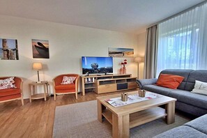 Ein modernes Wohnzimmer mit einem Flachbildfernseher, zwei Sofas, einem Couchtisch und einem Bücherregal.