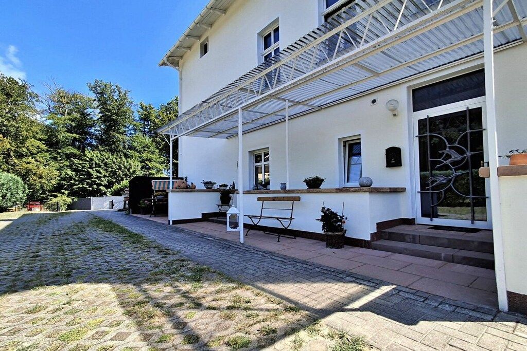 Ein zweistöckiges Gebäude mit einer überdachten Veranda, Blumentöpfen und einer Bank.