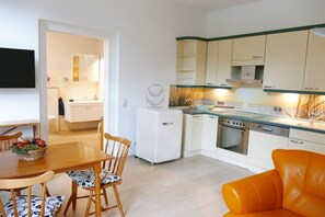 A compact kitchen with white cabinets, a built-in oven, and a dining area with a wooden table and chairs. - Fiedler holiday apartments (Heringsdorf (Seebad))