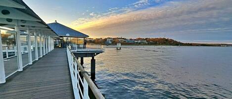 A wooden pier extending into a body of water with a covered seating area on one end.