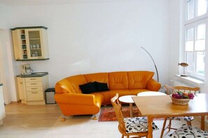 Een kamer met een bank, een eettafel, een kast en een raam.
