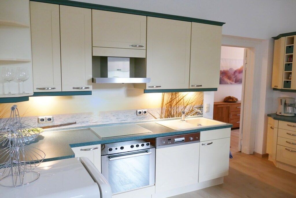 Una cocina compacta con horno integrado, lavavajillas y fregadero. Hay armarios sobre la encimera y una pequeña ventana al fondo.