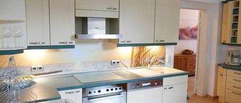 Una cocina compacta con horno integrado, lavavajillas y fregadero. Hay armarios sobre la encimera y una pequeña ventana al fondo.