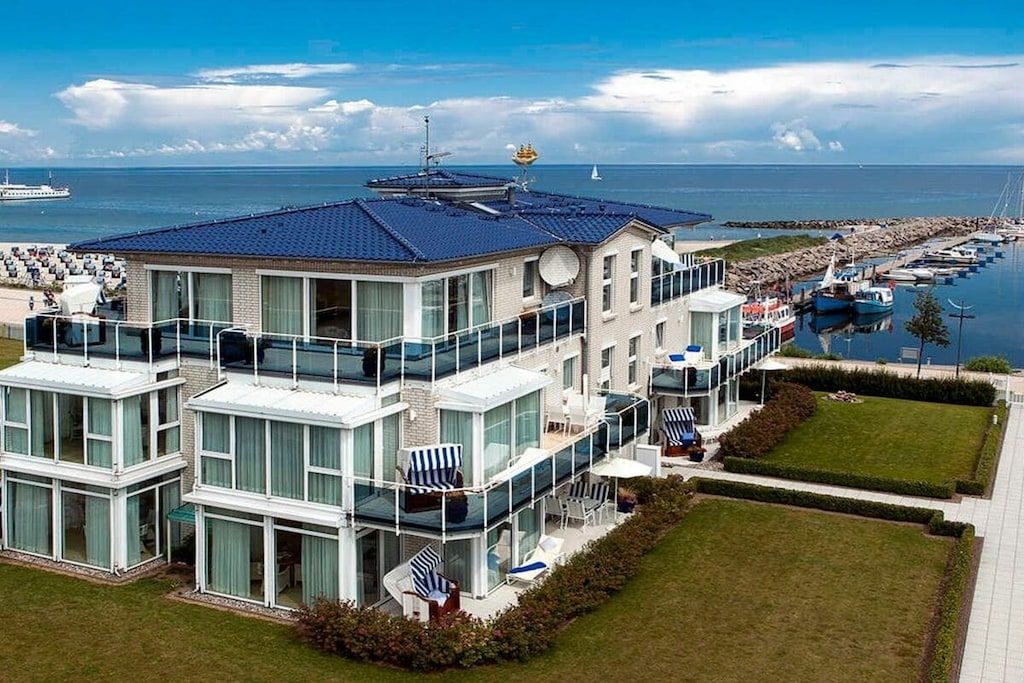 A modern multi-story building with large windows, a balcony, and a view of the sea.