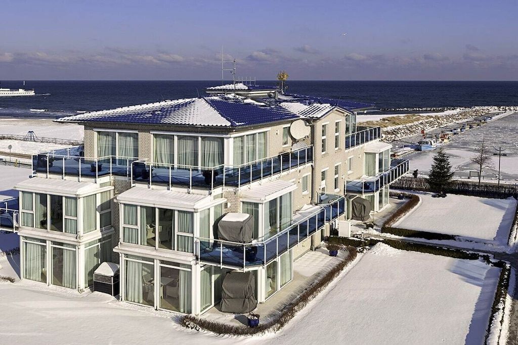 En moderne bygning med flere etager, store vinduer og balkoner med udsigt over en sneklædt strand.