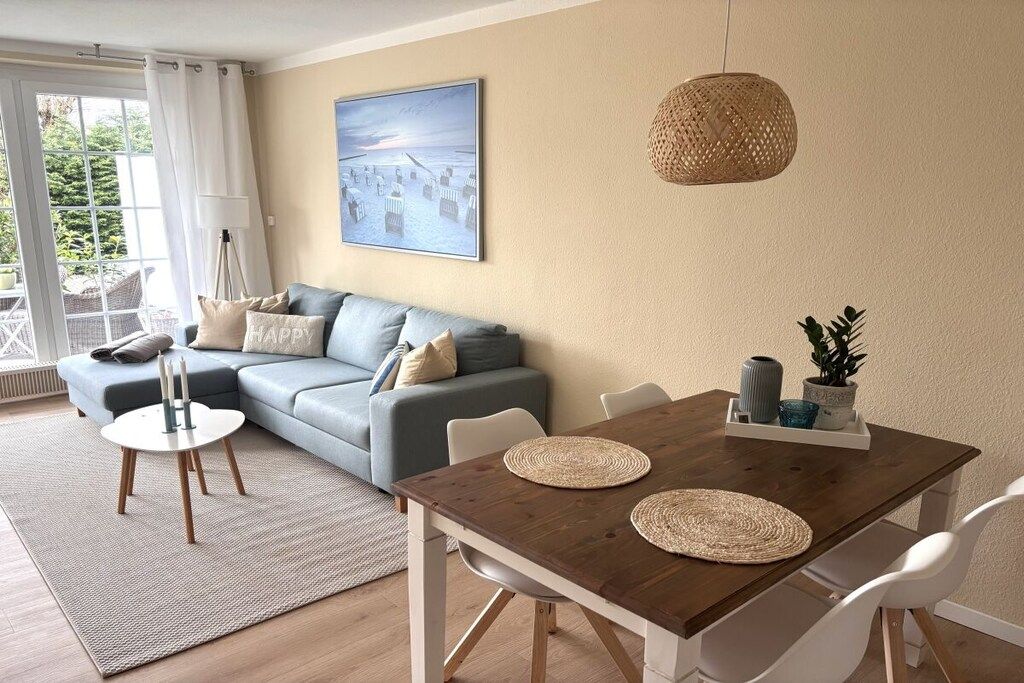 Ein modernes Wohnzimmer mit einer Couch, einem Esstisch mit Platzsets, einer Hängelampe und einem Bild an der Wand.