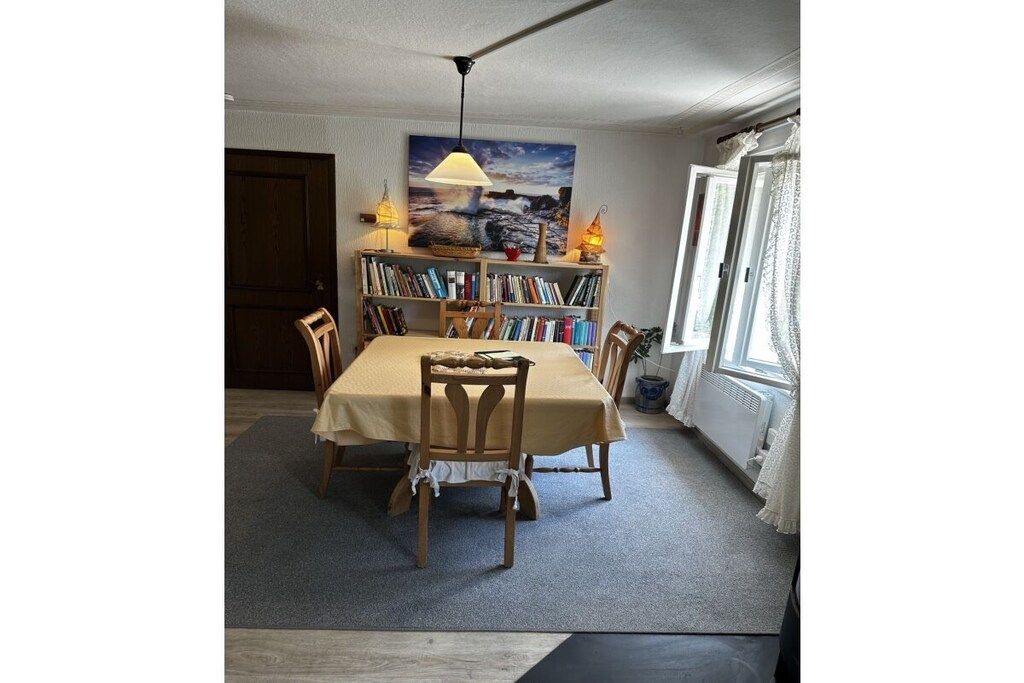 A dining area with a table, chairs, a bookshelf, and a painting on the wall.