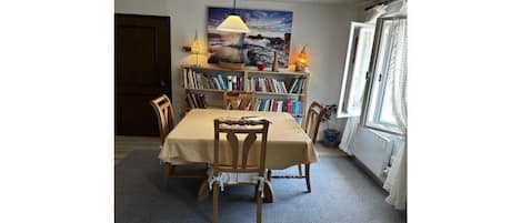 Un comedor con una mesa, sillas, una estantería y un cuadro en la pared.