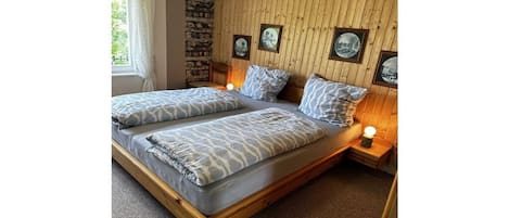 A double bed with a wooden frame and grey bedding, a stone wall, wooden paneling, and framed pictures on the wall.