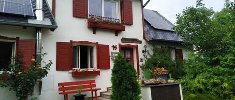 A two-story building with red shutters, a bench, and potted plants.