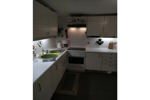 A compact kitchen with white cabinets, a stove, a sink, and a microwave.