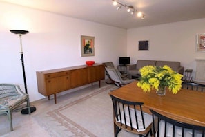 Un salon comprenant une table à manger en bois, un canapé, un téléviseur et un lampadaire.