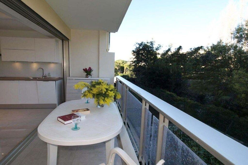 Een balkon met een tafel, stoelen, een plantje en uitzicht op bomen.