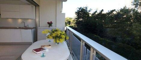 Een balkon met een tafel, stoelen, een plantje en uitzicht op bomen.