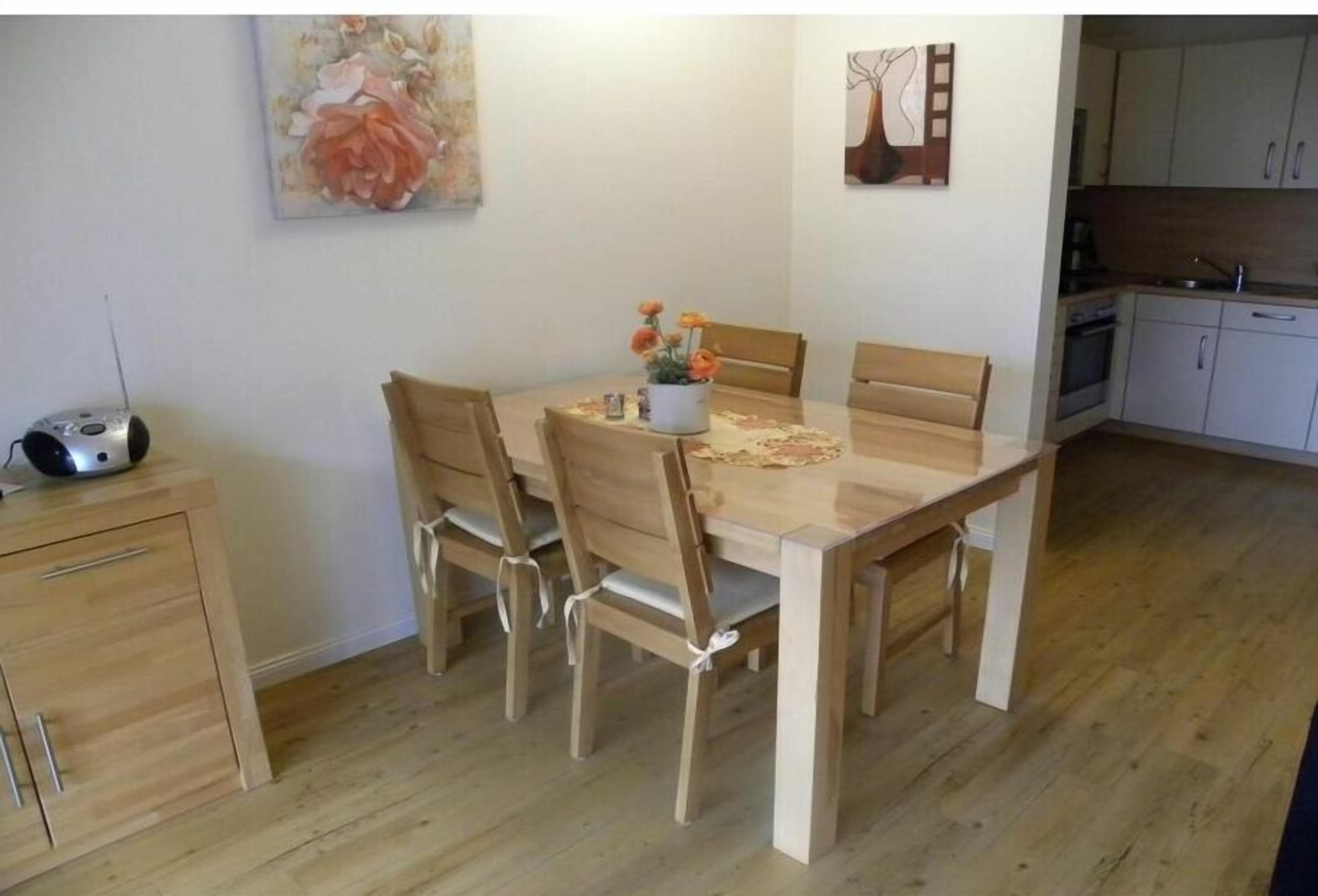 A dining area with a wooden table and chairs, a small cabinet, and a painting on the wall.
