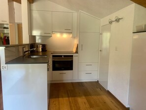 Una cocina compacta con gabinetes blancos, horno empotrado y lavamanos.
