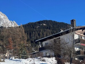 Eine Berglandschaft mit einem Gebäude im modernen Stil, umgeben von verschneitem Gelände und Bäumen.