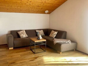 Ein modernes Wohnzimmer mit Holzboden, einem braunen Sofa mit gemusterten Kissen, einem kleinen Holztisch und einer Lampe.