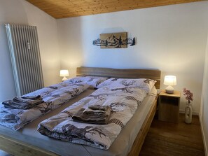 Ein Doppelbett mit gemustertem Bettbezug, zwei Nachttischlampen, ein Wandbild und eine Heizung.