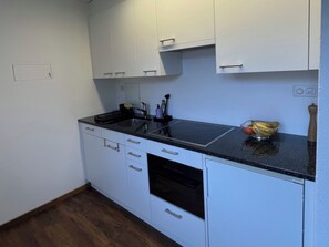 A compact kitchen with white cabinets, a black countertop, and a built-in oven. - Satin Home Appartement/Fewo, Bad, WC Studio - 3 Betten by Interhome (Savognin)