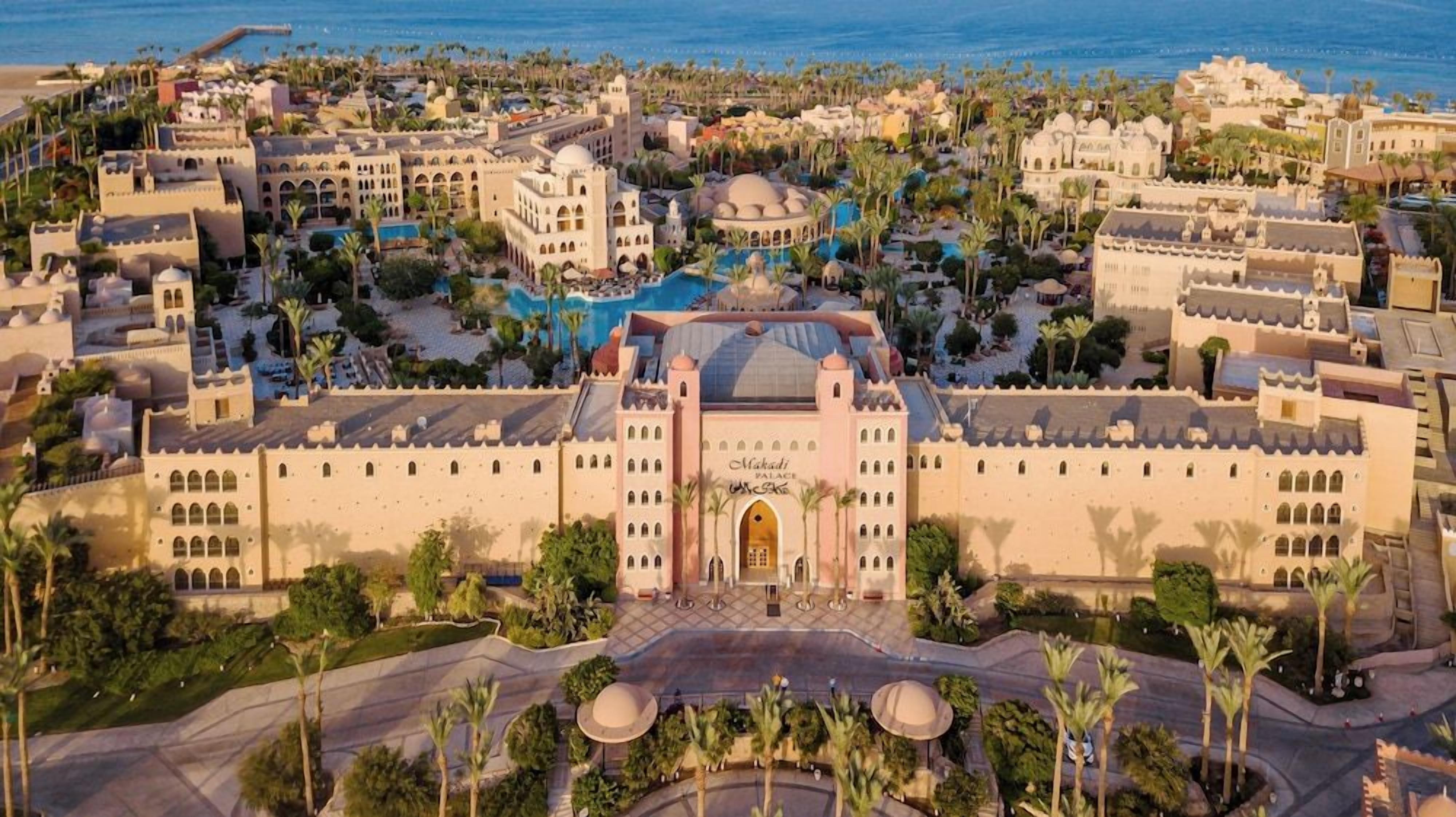 A large resort with multiple buildings, a central pool, and palm trees.