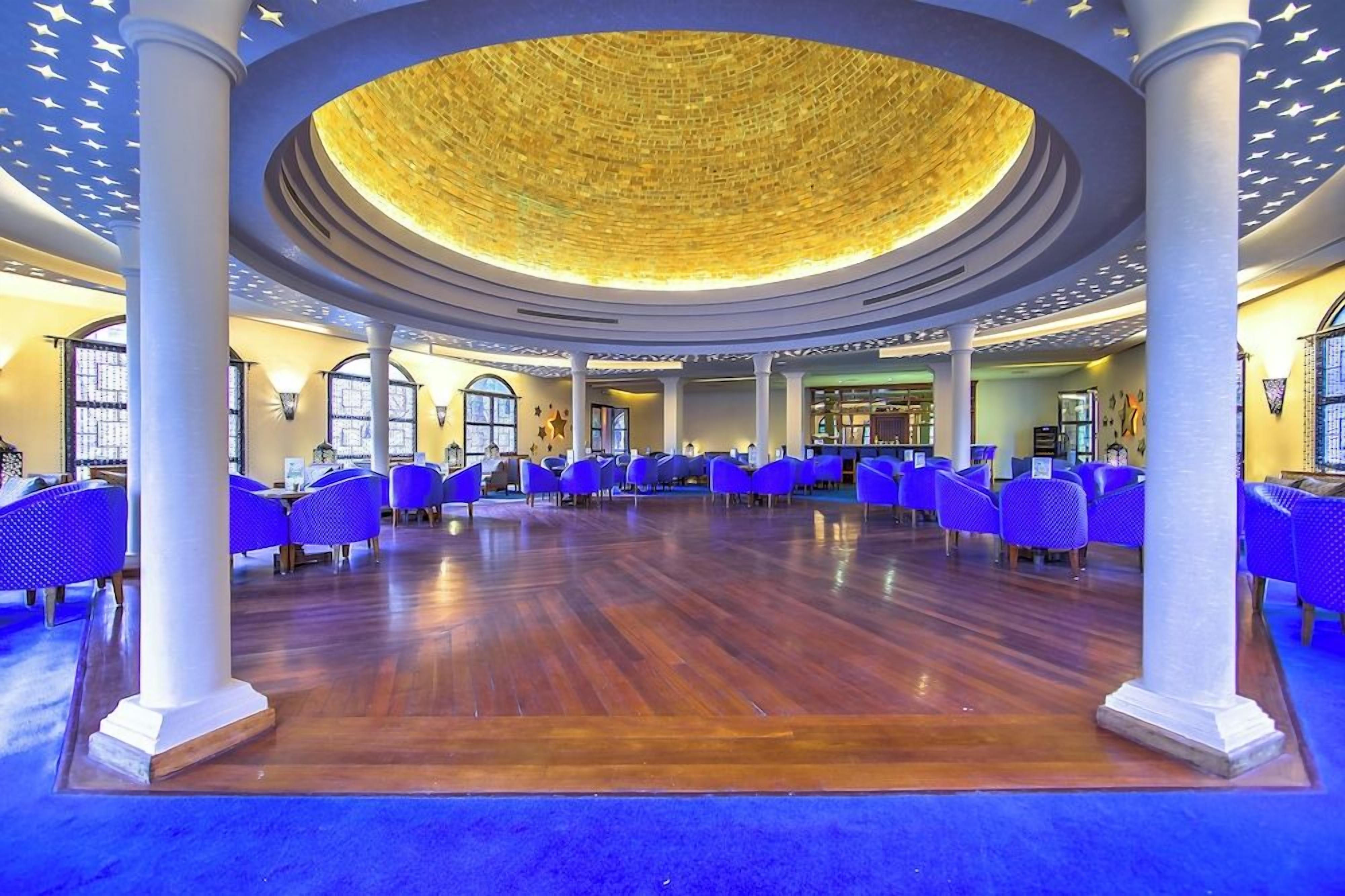 A spacious lobby with a high ceiling, circular skylight, and rows of blue chairs.