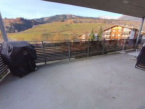 Varanda com vista para uma paisagem montanhosa, churrasqueira e um edifício com várias janelas.