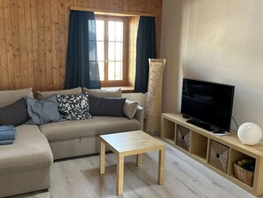 Ein modernes Wohnzimmer mit einer Couch, einem Couchtisch, einem Fernseher und einem Fenster mit Vorhängen.