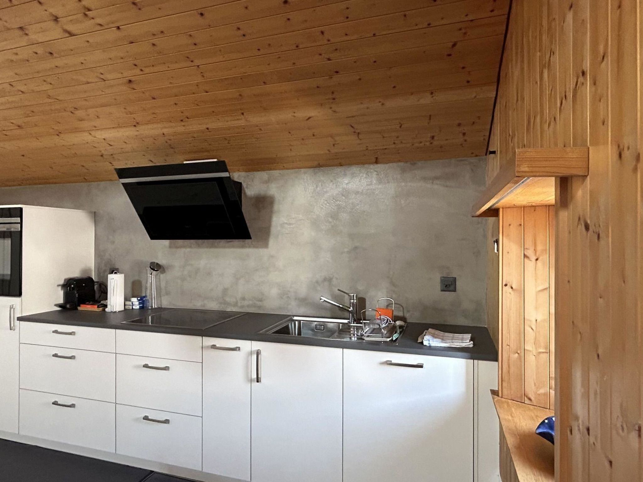 A modern kitchen with white cabinets, a black countertop, and a wooden ceiling.