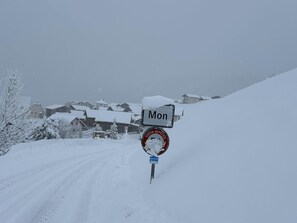Eine schneebedeckte Straße mit einem Schild, das 'Mon' anzeigt, und einem roten Kreis mit weißer Schrift.