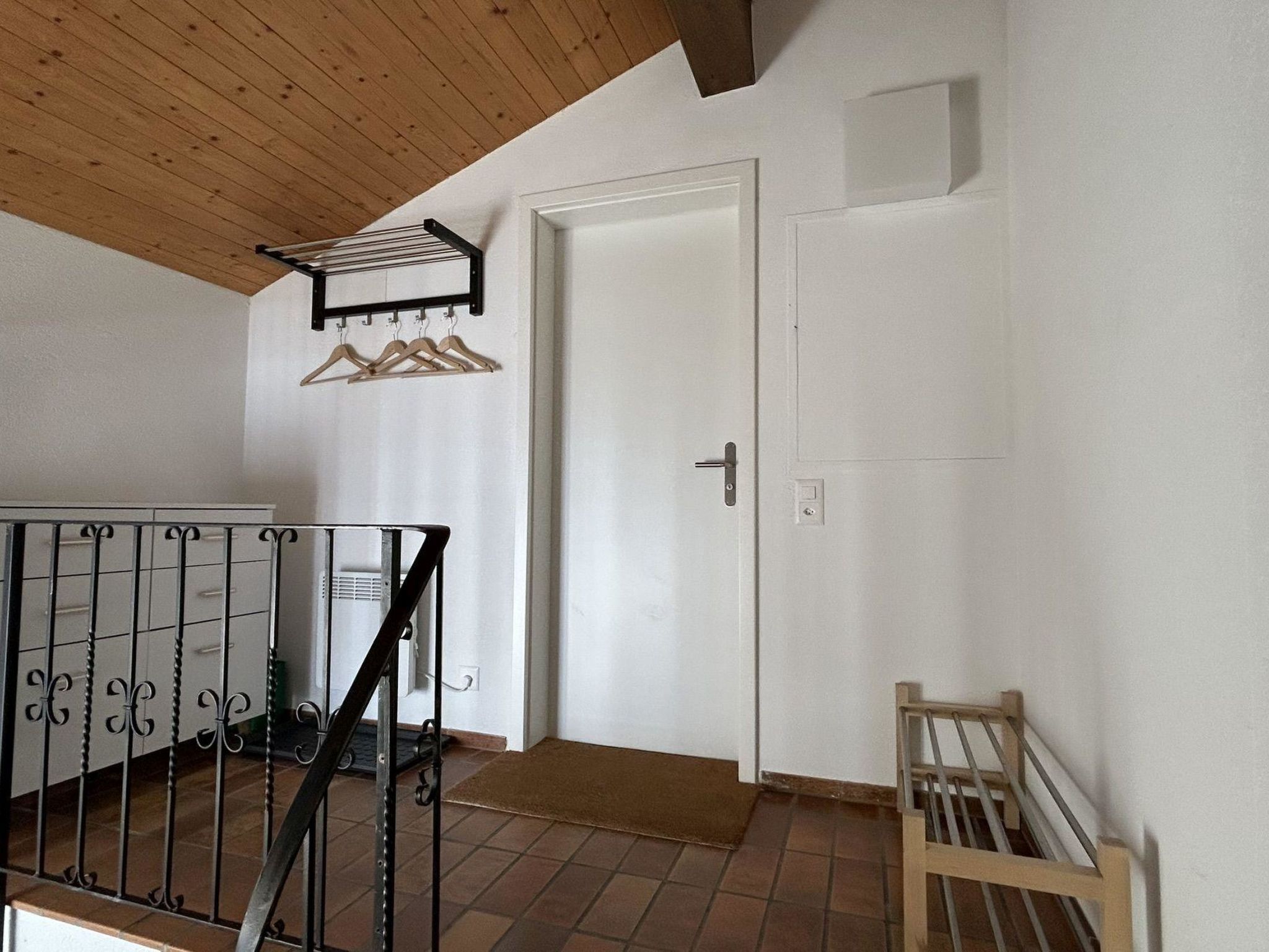 Une pièce avec un plafond en bois, une porte blanche, un portail en métal et un banc en bois.