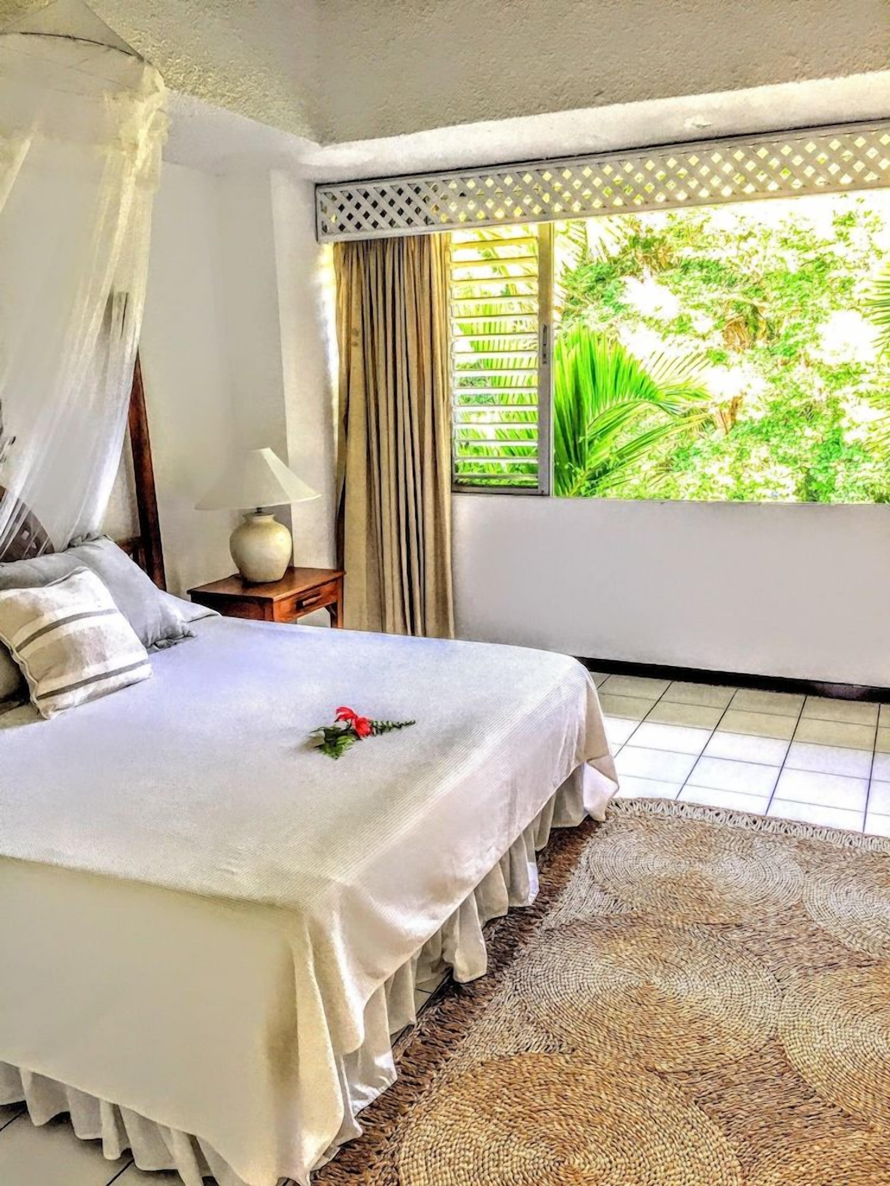 A bedroom with a bed, curtains, a window, and a view of greenery.